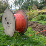 Wooden spool with fiber optic cable for fast internet ready to be laid in narrow trenches in the ground